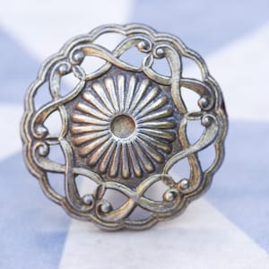 May include: A silver-toned metal decorative knob with a circular design featuring a central sunburst pattern and intricate scrollwork.