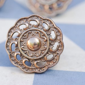 May include: A decorative, ornate, silver-toned metal knob with a detailed floral design. The knob has a circular shape with a raised centre.