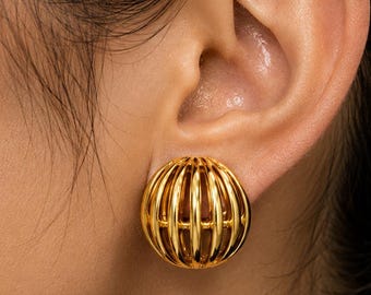 May include: A gold-toned earring featuring a spherical, cage-like design with vertical metal bars. The earring has a polished, reflective surface and a rounded, open-work structure that creates a distinct, dimensional appearance on the earlobe.
