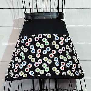 May include: Black apron with a pocket and a pattern of colorful eyes on the bottom half.