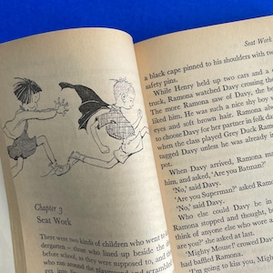以下が含まれることがあります： イラストとテキストが掲載された開いた本。左ページには、2人の子供が走っている白黒の絵が描かれています。右ページには「Seat Work」というタイトルと番号53のテキストが含まれています。
