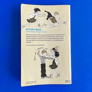 以下が含まれることがあります： 子供たちのイラストが描かれた、ヴィンテージの「A Puffin Book」の裏表紙。本のタイトルと著者が表示され、物語を説明するテキストも表示されます。表紙はクリーム色の背景に青色のテキストとイラストが描かれています。