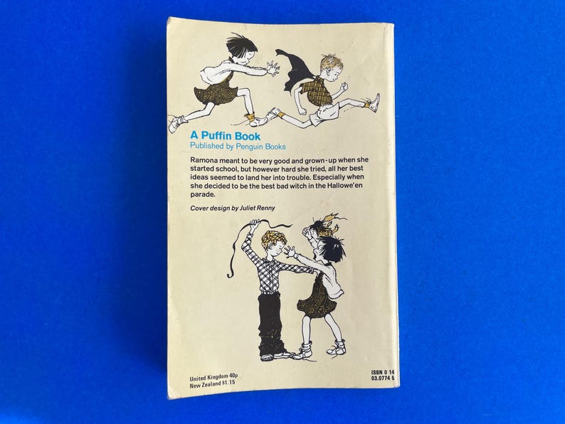 以下が含まれることがあります： 子供たちのイラストが描かれた、ヴィンテージの「A Puffin Book」の裏表紙。本のタイトルと著者が表示され、物語を説明するテキストも表示されます。表紙はクリーム色の背景に青色のテキストとイラストが描かれています。