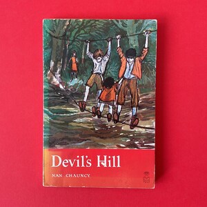 May include: A vintage book cover titled "Devil's Hill" by Nan Chauncy, featuring an illustration of three children on a rope bridge in a forest setting. The cover has a red banner with white text and is set against a red background.
