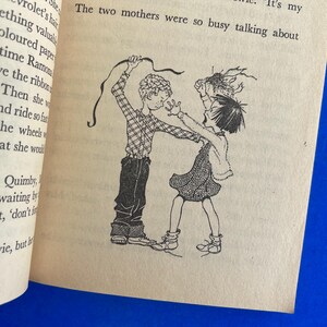 以下が含まれることがあります： 本からの白黒イラストで、2人の子供が描かれています。一人はリボンを持ち、もう一人は手を伸ばしています。画像はクリーム色のページにあり、テキストが表示されています。
