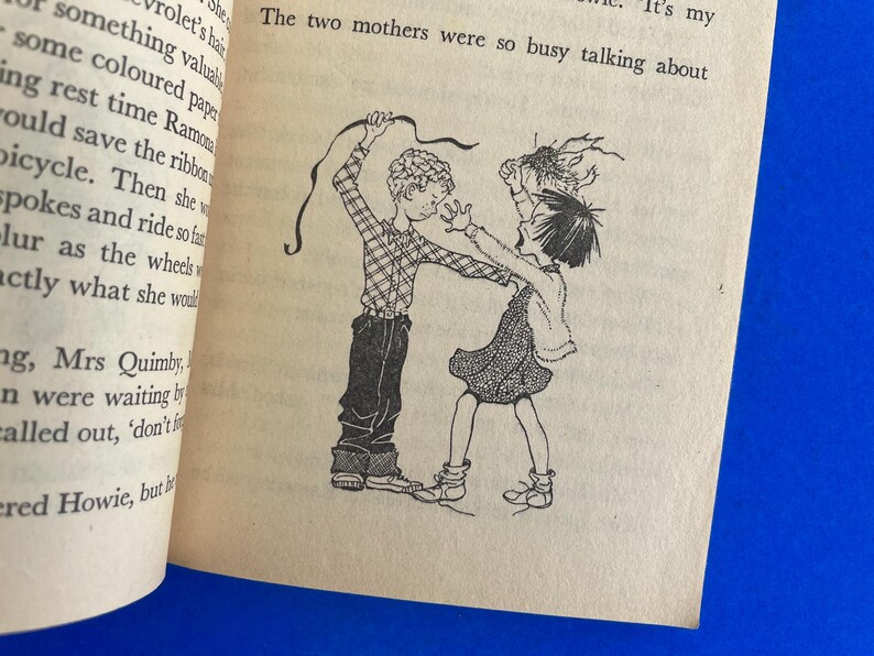 以下が含まれることがあります： 本からの白黒イラストで、2人の子供が描かれています。一人はリボンを持ち、もう一人は手を伸ばしています。画像はクリーム色のページにあり、テキストが表示されています。