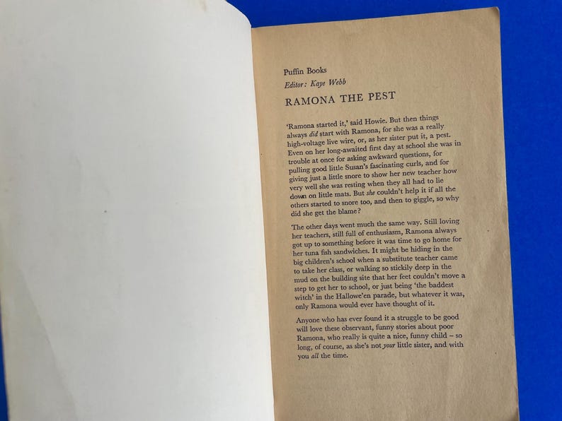 以下が含まれることがあります： Puffin Booksの「Ramona the Pest」からのテキストが書かれた開いた本。ページはオフホワイトで、黒い文字が書かれています。本は青い表面に開かれています。