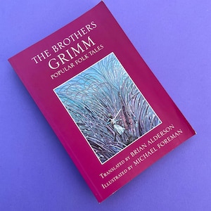 May include: A red book titled "The Brothers Grimm: Popular Folk Tales" with an illustration of a woman in a white dress standing in a field of tall purple grass. The book is translated by Brian Alderson and illustrated by Michael Foreman.