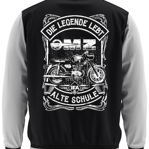 Può includere: Giacca college nera e bianca con maniche grigie. La parte posteriore presenta una grafica di moto con il testo "DIE LEGENDE LEBT" e "ALTE SCHULE". La giacca ha colletto, polsini e orlo a righe.