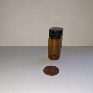 May include: A small amber glass bottle with a black screw-on lid. The bottle is about the size of a US penny.