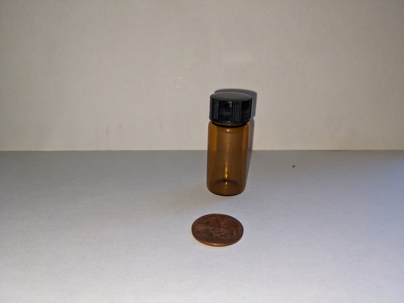 Peut inclure: Une petite bouteille en verre ambr&eacute; avec un bouchon &agrave; vis noir. La bouteille est &agrave; peu pr&egrave;s de la taille d'une pi&egrave;ce de 1 centime d'euro.