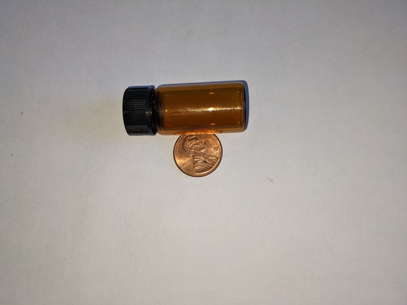 Peut inclure: Une petite bouteille en verre ambr&eacute; avec un bouchon &agrave; vis noir, &agrave; c&ocirc;t&eacute; d'une pi&egrave;ce de monnaie am&eacute;ricaine.