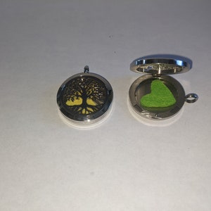 May include: Two silver metal essential oil diffusers, one with a tree of life design and the other with a green heart-shaped pad inside.