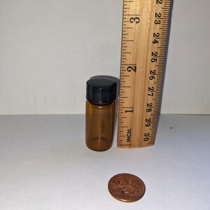 Peut inclure: Une petite bouteille en verre ambr&eacute; avec un bouchon &agrave; vis noir. La bouteille mesure environ 5 cm de haut et est &agrave; c&ocirc;t&eacute; d'une r&egrave;gle qui montre que la bouteille mesure environ 3,8 cm de haut. Une pi&egrave;ce de monnaie est &eacute;galement dans l'image pour l'&eacute;chelle.