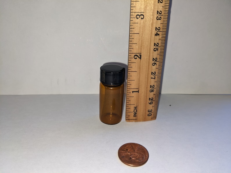 Peut inclure: Une petite bouteille en verre ambr&eacute; avec un bouchon &agrave; vis noir. La bouteille mesure environ 5 cm de haut et est &agrave; c&ocirc;t&eacute; d'une r&egrave;gle qui montre que la bouteille mesure environ 3,8 cm de haut. Une pi&egrave;ce de monnaie est &eacute;galement dans l'image pour l'&eacute;chelle.