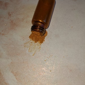 Peut inclure: Un petit flacon en verre ambr&eacute; avec de la poudre m&eacute;tallique dor&eacute;e qui se r&eacute;pand de son ouverture.