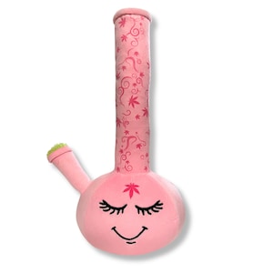 May include: Pink plush bong with a smiling face and pink and white floral design. The bong has a green mouthpiece and a leaf design on the front.