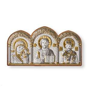 Puede incluir: Icono religioso con tres paneles, con detalles plateados y dorados. Los paneles representan figuras religiosas con halos, sobre un fondo ornamentado. El icono tiene un borde marrón.