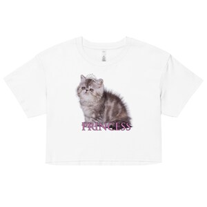 May include: White crop top featuring a gray and brown kitten wearing a tiara and pearl necklace. The word "PRINCESS" is printed in purple below the kitten. The shirt is made of a soft material.