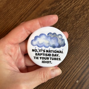 May include: A white button with a watercolor image of blue clouds and rain. The text reads, "NO, IT'S NATIONAL BAPTISM DAY. TIE YOUR TUBES, IDIOT."