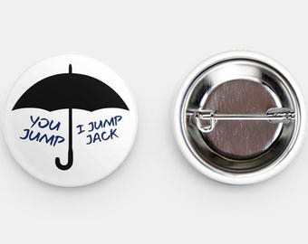 May include: Two white round buttons. One button features a black umbrella graphic with the text "You Jump, I Jump Jack" in blue. The other button shows the back with a metal pin.