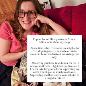 May include: A person wearing glasses and a pink shirt smiles, holding a note with text about their shop. The note mentions free shipping and thanks customers for their support of small businesses.