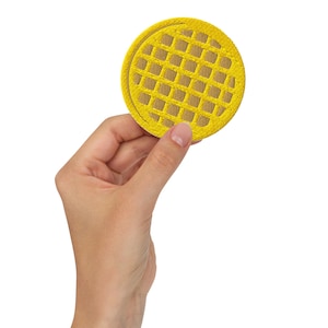 May include: A yellow embroidered waffle patch, held against a white background. The patch has a detailed grid pattern and a slightly darker yellow interior. The round patch has a raised edge. The patch is approximately 7.6 cm in diameter.