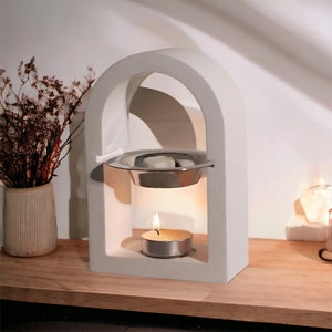 Könnte beinhalten: Weißer, keramik-archförmiger Räucherofen mit einer silbernen Metallschale und einer kleinen weißen Kerze. Der Ofen steht auf einer Holzoberfläche.