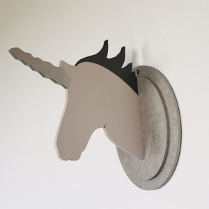 May include: A beige wooden unicorn head wall decoration with a black mane and a twisted horn. The unicorn head is mounted on a round, silver-grey wooden base.