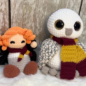 May include: Two crocheted stuffed toys, a white owl with a burgundy and gold scarf and a red-haired human figure with a black robe and a burgundy and gold scarf holding a wand.