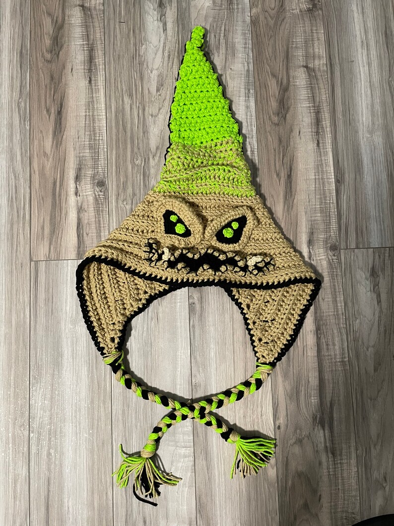 May include: A crocheted hat with a green and brown pointed top and a black and brown braided tie. The hat features a scary face with green eyes and a black mouth.