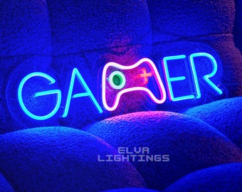 May include: A neon sign displaying the word GAMER in bright blue, with the letter M replaced by a pink and white outline of a video game controller featuring a green circular button and a yellow cross-shaped button on its face.