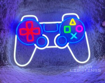 May include: A neon sign shaped like a video game controller with a white outline. The left side features a red directional pad, while the right side displays a yellow triangle, green square, pink circle, and blue cross. The text ELVA LIGHTINGS is visible.
