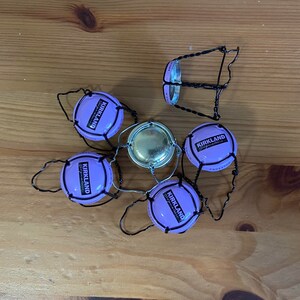 Op de afbeelding: Vijf paarse en zwarte draad champagne flessenstoppers met het woord "KIRKLAND" erop gedrukt.