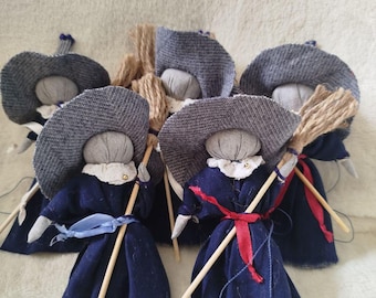 May include: Five handmade fabric witch dolls with gray hats, blue dresses, and wooden broomsticks. The dolls are arranged in a circle on a white fuzzy surface.