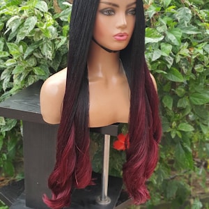 May include: A long black and burgundy ombre wig with a lace front. The wig is styled in small braids and is displayed on a mannequin head.