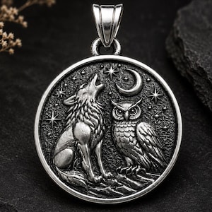 May include: A circular silver pendant featuring a raised relief design of a wolf howling at a crescent moon and a perched owl. The background is textured with small stars, and the piece includes a polished silver bail at the top for hanging.