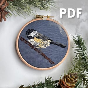 Könnte beinhalten: Stickerei-Hoop-Kunst mit einem schwarz-weißen Vogel mit gelben und weißen floralen Details auf einem dunkelblauen Stoffhintergrund. Der Reifen ist aus Holz und hat eine natürliche Oberfläche.