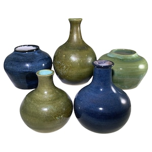 May include: Five ceramic vases in shades of blue and green. The vases vary in shape, with some having a rounded body and others a more elongated form. The glazes have a speckled or mottled appearance, adding texture to the pieces. The vases are displayed against a white background.