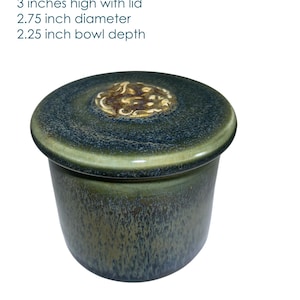 May include: Antique glass pot with lid. The pot is 3 inches high, 2.75 inches in diameter, and has a 2.25-inch bowl depth. The pot is a dark teal color with a gold-colored design on the lid. The text "Pot D: Antique Glass" is visible.