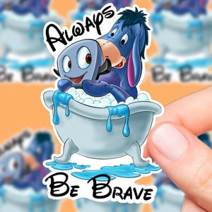 Op de afbeelding: Een blauw en grijs cartoonfiguur, Eeyore, zit in bad met een blauwe broodrooster. De broodrooster heeft een glimlachend gezicht en houdt een blauwe zeepstaaf vast. De tekst "Always Be Brave" is geschreven in wit cursief schrift.