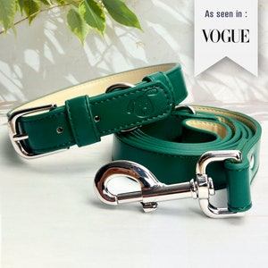 Puede incluir: Un juego de collar y correa para perro de cuero verde con hebilla y cierre plateados. El collar tiene una pequeña huella de pata de perro grabada. El texto "As seen in: VOGUE" es visible en la esquina superior derecha de la imagen.