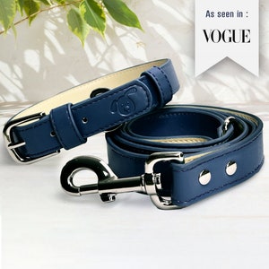 Pode incluir: Um conjunto de coleira e trela para cães de couro azul com fivela e fecho prateados. A coleira tem uma pequena silhueta de cão em relevo. A trela tem dois rebites prateados. Visto em: VOGUE