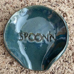 May include: A teal blue ceramic spoon rest with the word "SPOON'" embossed on the surface.