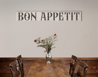 Puede incluir: Un letrero de madera con las palabras "BON APPETIT" en letras negras cuelga sobre una mesa de madera. Un jarrón plateado con vegetación y bayas rojas se encuentra sobre la mesa, con dos sillas de madera a cada lado.
