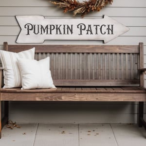 May include: A wooden bench with two white pillows and a sign that reads "PUMPKIN PATCH". The bench is surrounded by fall decorations, including a pumpkin, flowers, and a lantern, creating a cozy autumn scene.