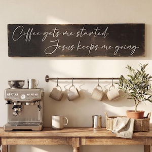 May include: A rustic wooden sign with the text "Coffee gets me started. Jesus keeps me going." hangs above a coffee station. A stainless steel espresso machine, mugs, and a small plant are on a wooden table.