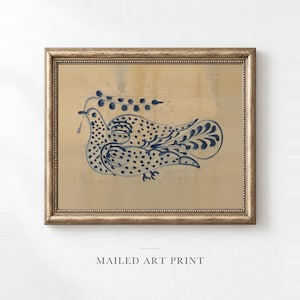 May include: A framed art print featuring a dark blue ink illustration of a stylized bird with dotted patterns and a leafy branch above it. The artwork is set against a light tan, textured background and enclosed in a metallic gold frame.
