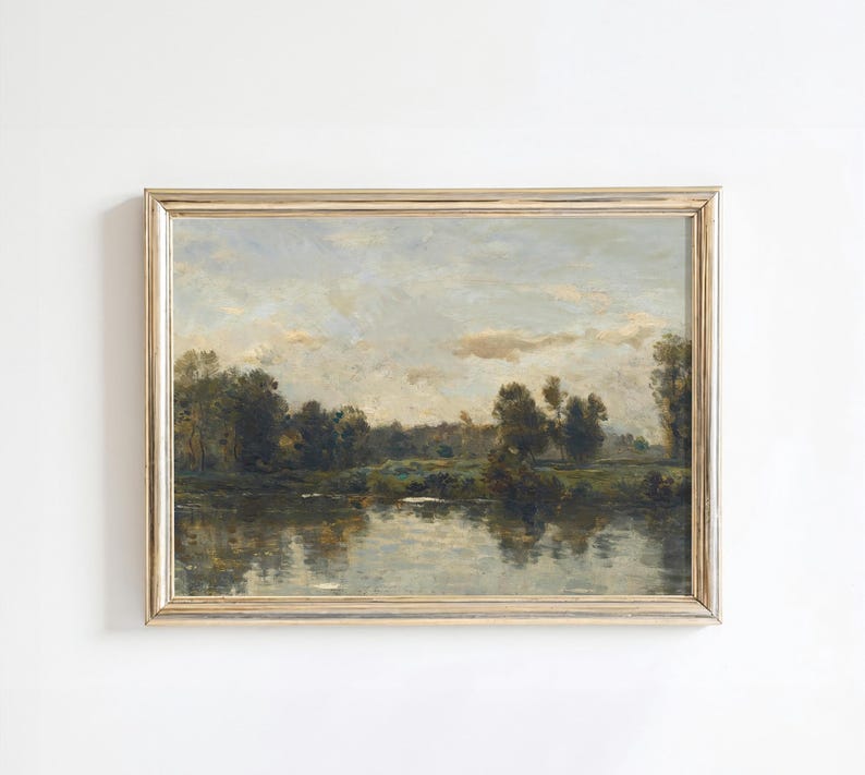 May include: A framed landscape painting depicting a river scene with trees and a cloudy sky. The painting is in a gold frame and has a rustic, vintage feel.