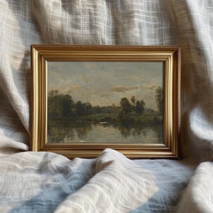 May include: A framed landscape painting depicting a river scene with trees and a cloudy sky. The frame is gold with a decorative border.